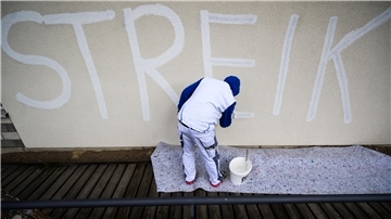 Ein Maler überstreicht das Wort Streik mit weißer Farbe.