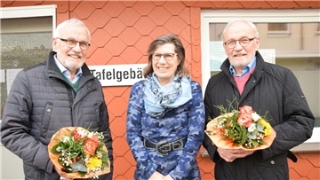 Zwei Männer mit Blumensträußen und eine Frau