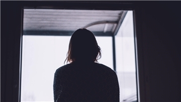 Frau als Silhouette von hinten vor einem Fenster.