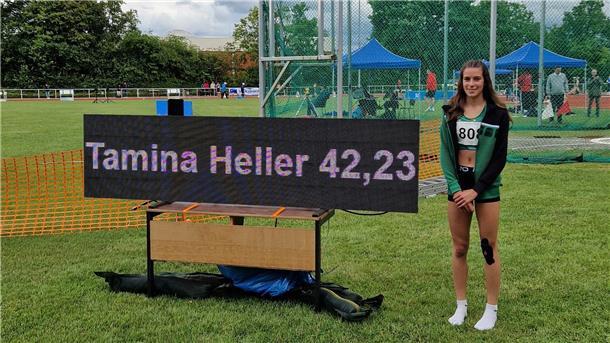 Tamina Heller steht auf dem Sportplatz neben der Anzeigetafel, die ihre Rekordzeit von 42,23 Sekunden über 300 Meter Hürden zeigt.
