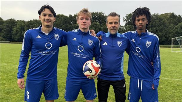 Vier Männer in blauer Sportkleidung. Einer hält einen Fußball in der Hand.