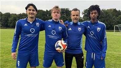 Vier Männer in blauer Sportkleidung. Einer hält einen Fußball in der Hand.