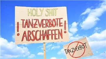  Schilder mit der Aufschrift "Tanzverbote abschaffen" und "Tanzverbot" sind bei der Demo gegen das Tanzverbot an Stillen Tagen vor weißblauem Himmel auf der Theresienwiese zu sehen. 