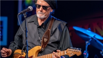 Ein Mann am Mikrofon mit einer Gitarre. Blues-Musiker Tas Cru spielt in der Jahnhalle. 