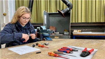 Eine junge Frau hält in der rechten Hand eine Zange, Sie arbeitet an einem Elektrostecker.