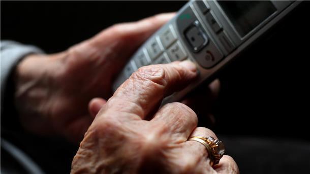 Eine ältere Frau hält ein schnurloses Festnetztelefon in der Hand. 