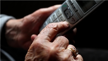 Eine ältere Frau hält ein schnurloses Festnetztelefon in der Hand. 