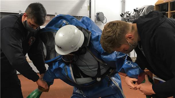Theorie-Stunde bei der Freiwilligen Feuerwehr von Düring: Der Einsatz im Chemikalien-Schutzanzug. Gruppenführer Sebastian Guderian (links) und Marc Wahlers (rechts) helfen Leon Jack Schröder beim Anziehen.