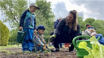 Thies (4) und Bennet (4) arbeiten in Teamwork. Einer gießt Wasser ins Loch, der andere setzt die Pflanze hinein. Erzieherin Jana Steffens unterstützt die beiden Acker-Racker.