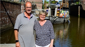 Ein älteres Paar steht an einem Hafenbecken vor einem Schiff. 