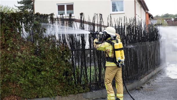 Ein Feuerwehrmann löscht eine zu großen Teilen bereits verbrannte Hecke.