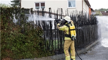 Ein Feuerwehrmann löscht eine zu großen Teilen bereits verbrannte Hecke.