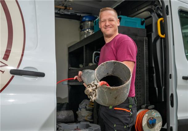 Ein Mann mit einem Abwasserrohr. Er steht vor einem Lieferwagen.