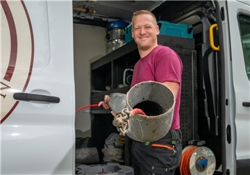 Ein Mann mit einem Abwasserrohr. Er steht vor einem Lieferwagen.