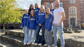 Eine Gruppe Schülerinnen posiert auf einem Schulhof mit dem Lehrer für ein Gruppenfoto.