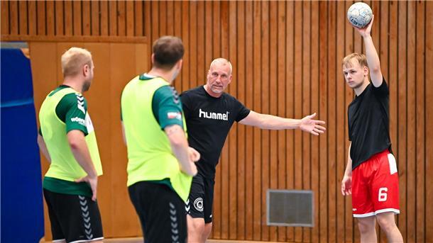 Ein Handballtrainer steht zwischen drei Handballspielern und erklärt einen Spielzug.