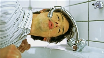 Mann trinkt Wasser aus dem Wasserhahn