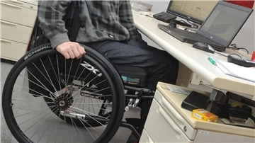 Mann sitzt mit Rollstuhl am Schreibtisch. 