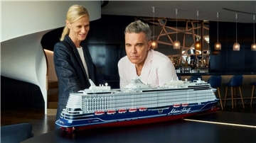 Frau und Robbie Williams sehen sich ein Modell eines Kreuzfahrtschiffes an