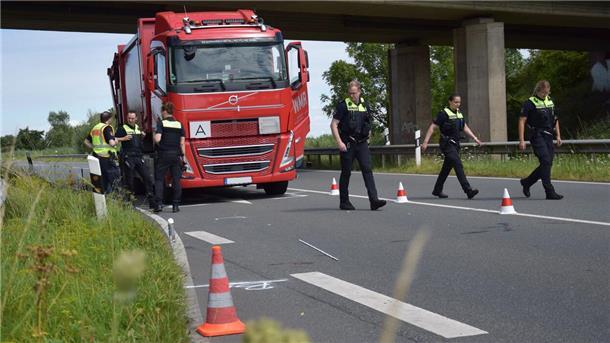 Ein Lkw steht auf einer Bundesstraße, davor sind mehrere Polizisten zu sehen.