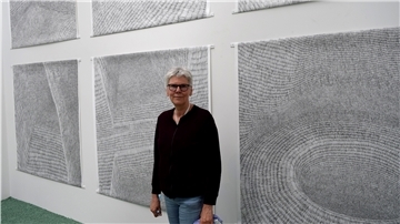 Ingeborg Dammann-Arndt steht vor sechs großen Grafiken die mit schwarzen Strichen bedruckt sind.
