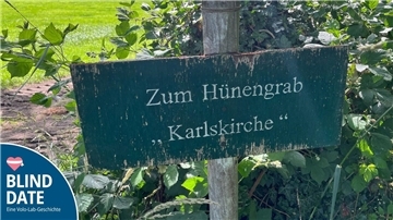 Wegweiser neben einem Feld. Zu lesen ist darauf: zum Hünengrab „Karlskirche“.
