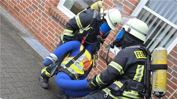 Unter Atemschutz bergen die Feuerwehrleute eine bewusstlose Person aus dem völlig verrauchten Gebäude.