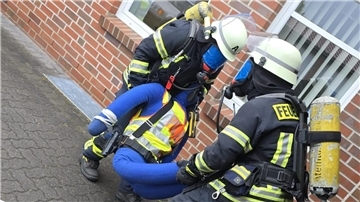 Unter Atemschutz bergen die Feuerwehrleute eine bewusstlose Person aus dem völlig verrauchten Gebäude.