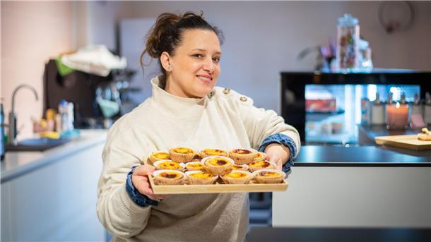 Eine Frau im weißen Pullover hält ein Tablett mit Pastéis de Nata, einem portugiesischem Gebäck, in der Hand.
