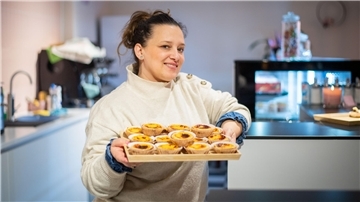 Eine Frau im weißen Pullover hält ein Tablett mit Pastéis de Nata, einem portugiesischem Gebäck, in der Hand.
