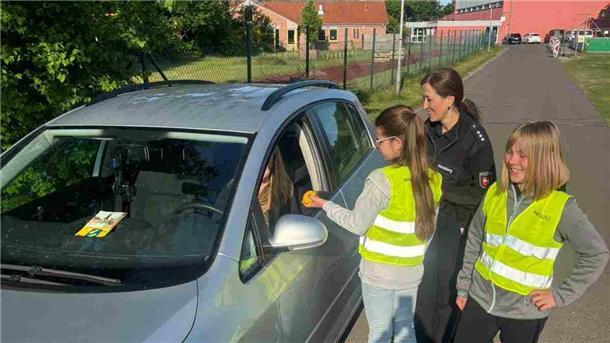 Kinder verteilen Zitronen bei Polizeiaktion in Nordholz Zwei Schülerinnen in Warnwesten überreichen einer Autofahrerin eine Zitrone, begleitet von einer Polizistin, im Rahmen einer Verkehrssicherheitsaktion.