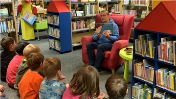 Kinder sitzen in der Bücherei und hören einer Frau zu, die ihnen aus einem Buch etwas vorliest. 