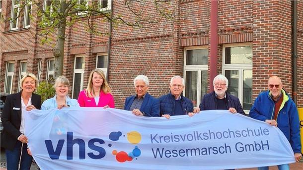 Die Geschäftsführung und die Gesellschafter der Kreisvolkshochschule Wesermarsch halten vor der zukünftigen Geschäftsstelle in Nordenham ein Banner in die Kamera.
