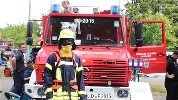 Kinder und Feuerwehrleute tummeln sich um ein Tanklöschfahrzeug. 