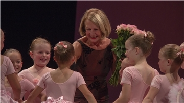 Eine Frau mit Rosen in der Hand inmitten von kleinen Ballettschülerinnen