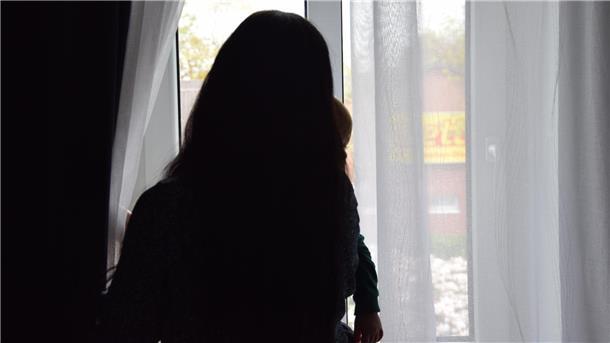 Eine Frau steht am Fenster und sieht mit ihrem Kind nach draußen. 