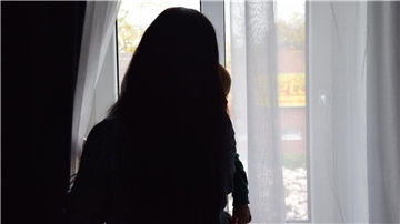 Eine Frau steht am Fenster und sieht mit ihrem Kind nach draußen. 