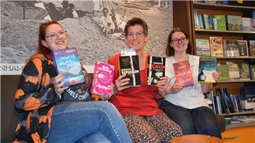 Drei Frauen sitzen auf einem Sofa und halten Bücher in den Händen. 