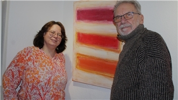 Ein Mann und eine Frau stehen vor einem Bild an der Wand.  Auf dem Bild sind dicke rote Balken in unterschiedlichen Rottönen.