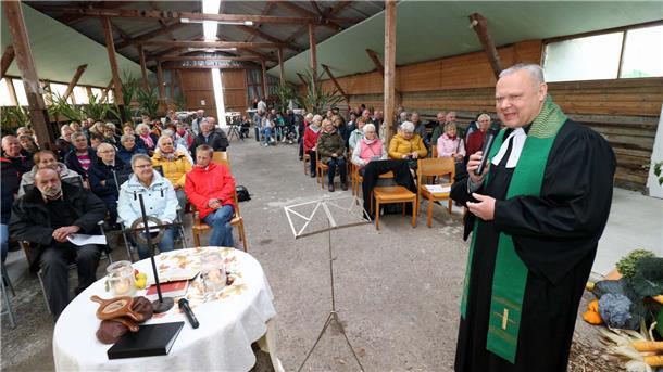 Pastor Clemens Bloedhorn spricht beim Erntedankgottesdienst in einer festlich geschmückten Bauernhofhalle in Sandstedt vor rund 150 Besucherinnen und Besuchern.