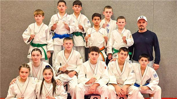 Judoka posieren in ihren Anzügen und mit Medaillen um den Hals für die Kamera.