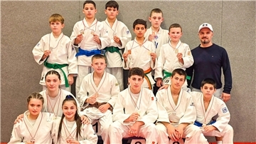 Judoka posieren in ihren Anzügen und mit Medaillen um den Hals für die Kamera.