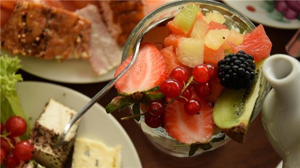 Etwas Joghurt mit Obst, eine Käseplatte sowie etwas Lachs stehen auf einem Frühstückstablett. 