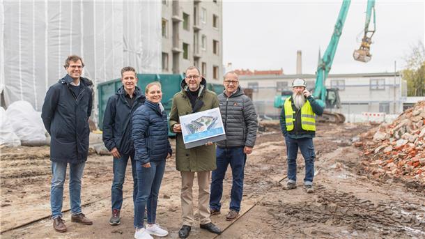 Mehrere Personen stehen auf einer Baustelle in Bremerhaven. Im Hintergrund sind ein Longfront-Abbruchbagger und ein Gebäude zu sehen. 