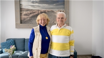 Eine Frau und ein Mann stehen in einem Wohnzimmer vor einem Bild, welches Strand und Meer zeigt.