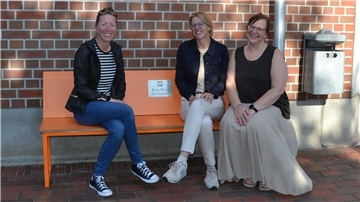 Drei Frauen sitzen auf der orangefarbenen Bank.