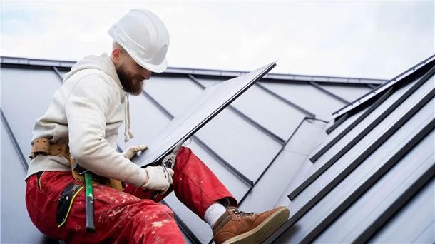Ein Arbeiter installiert auf einem Hausdach eine Photovoltaikanlage