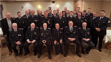 Gruppenbild von Feuerwehrkameraden der Freiwilligen Feuerwehr Loxstedt in Uniform, aufgenommen bei der Ehrungsveranstaltung in einem festlich dekorierten Saal. In mehreren Reihen sitzen und stehen die geehrten Mitglieder sowie Führungskräfte.