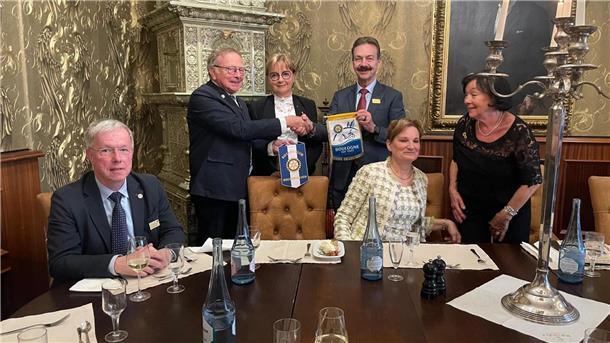Männer und Frauen in einem Raum. Zwei Männer tauschen Geschenke aus.