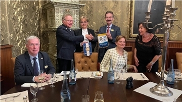 Männer und Frauen in einem Raum. Zwei Männer tauschen Geschenke aus.